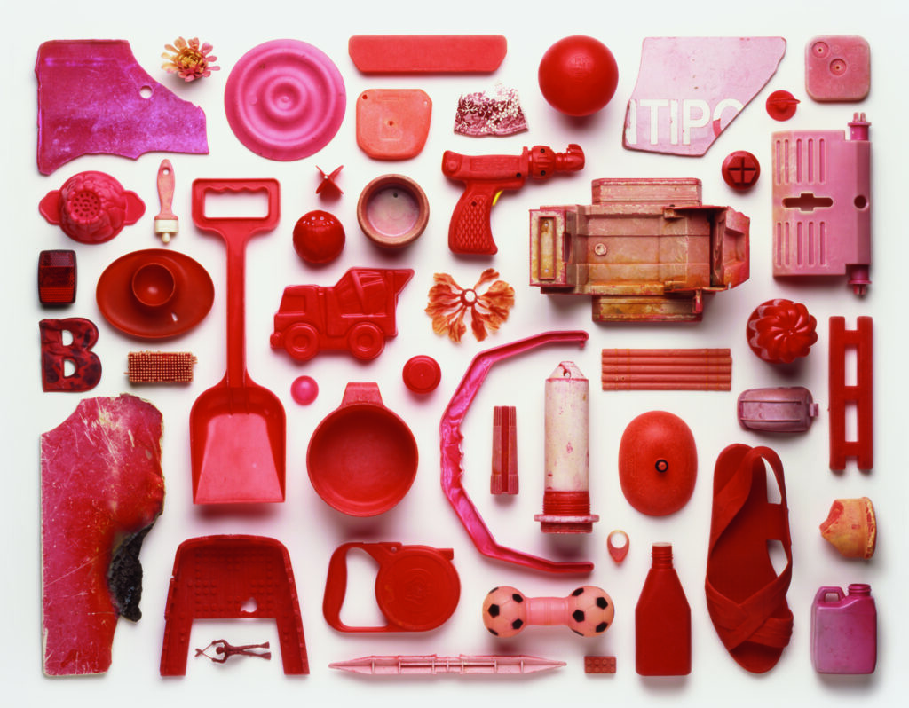 View from above of an artwork that is an arrangement of red-coloured pieces of plastic pollution washed up on a beach in the UK