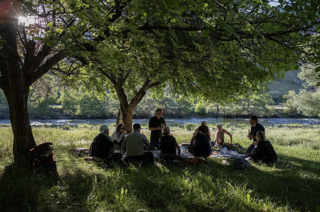 People sitting on grass by a river tasting wine in Georgia