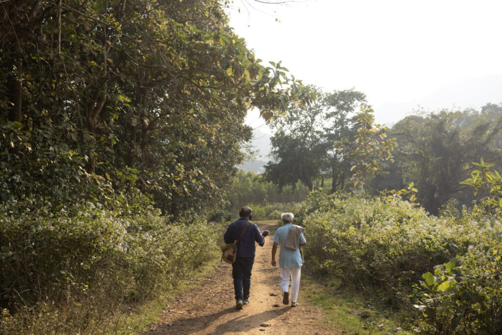rear view of Dr Debal Deb and dan Saladino, microphone in hand, walking down a path