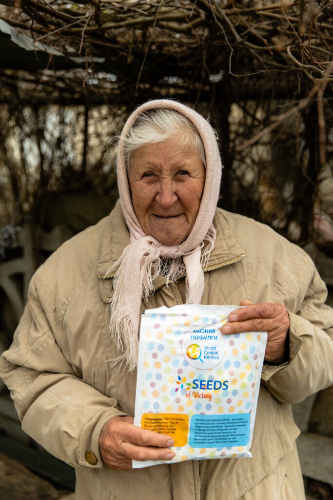 Portrait of a Ukrainian woman in a headscarf holding a packet of seeds from World Central Kitchen