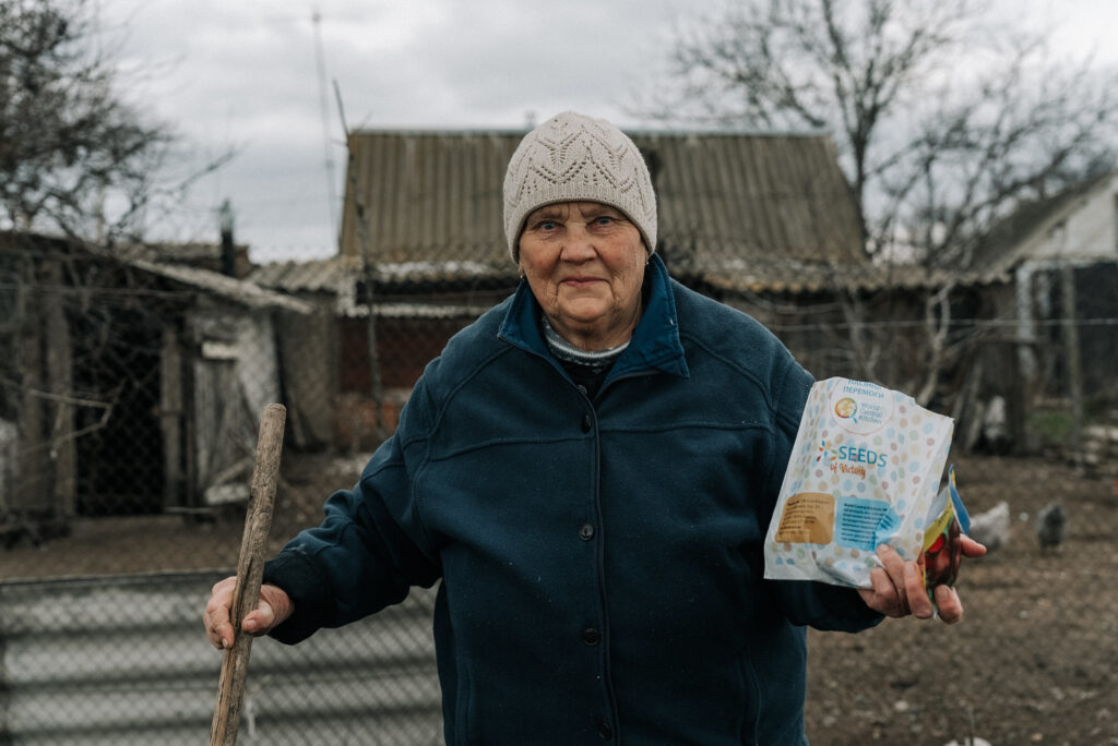 Portrait of a Ukrainian woman in a woolly hat holding a packet of seeds from World Central Kitchen