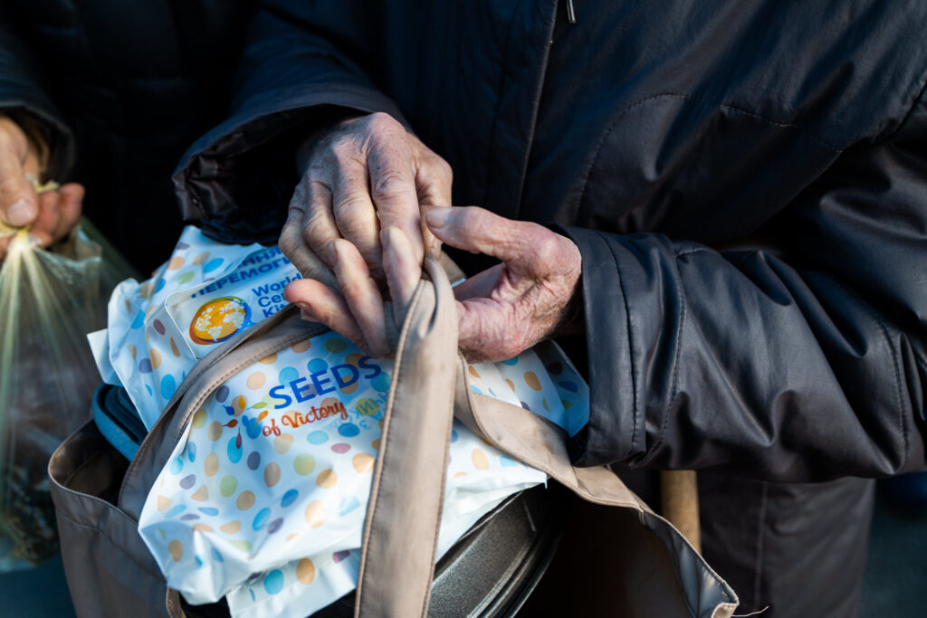 Portrait of an old Ukrainian woman's hands holding shopping bag containing packets of seeds from World Central Kitchen