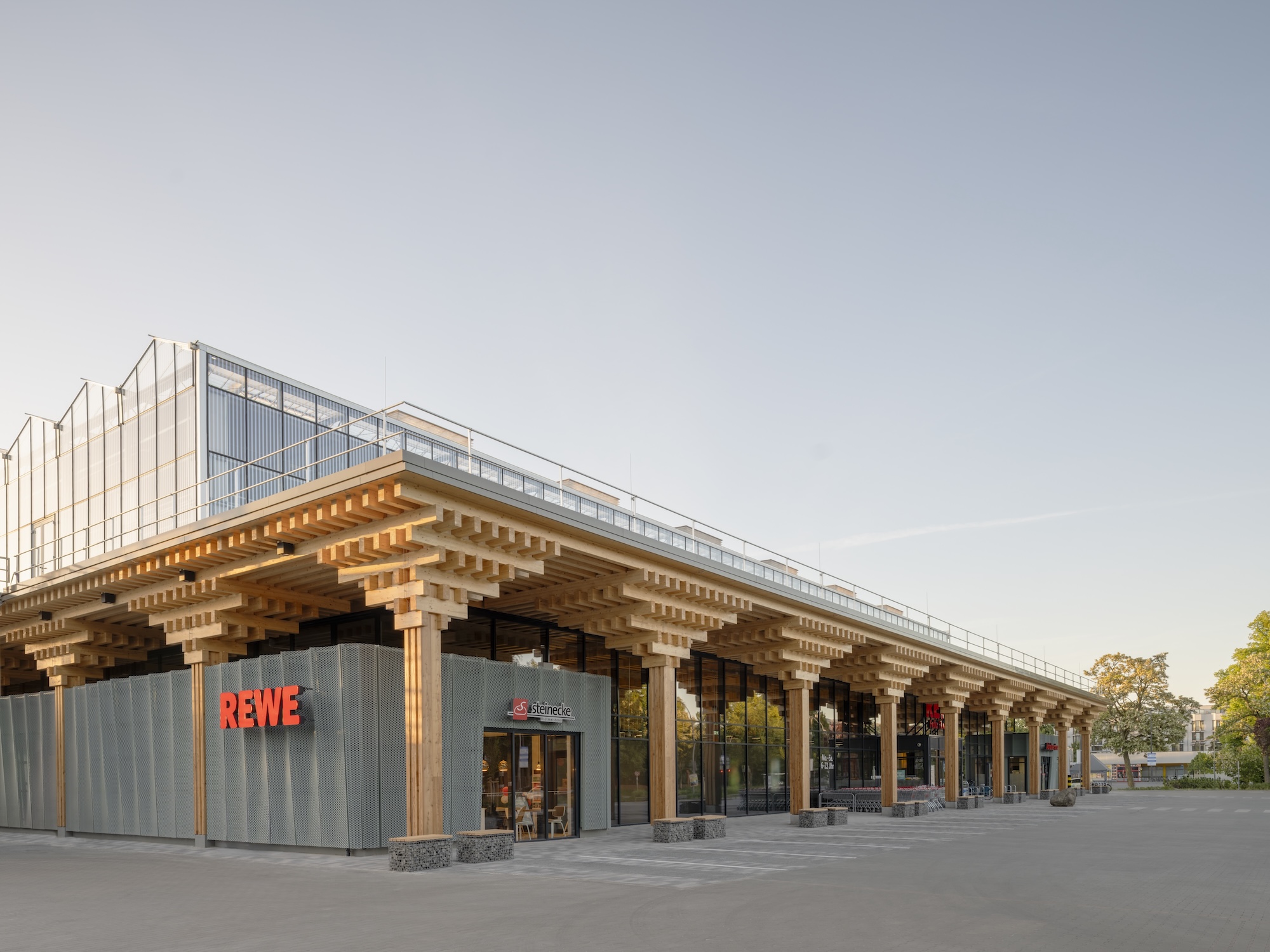 Exterior view of the Rewe Green Farming supermarket in Berlin-Lankwitz opened in May 2026 with the expectation that this construction form will become standard for the company going forward. The intention, says head of Construction Klaus Wiens, is to build around 10 per cent of new stores with a farm, and 90-plus per cent as standard stores without one. Image © Fritz Brunier, courtesy Acme.